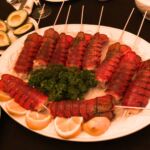Nine lobster tails on a white plate with lemon wedges